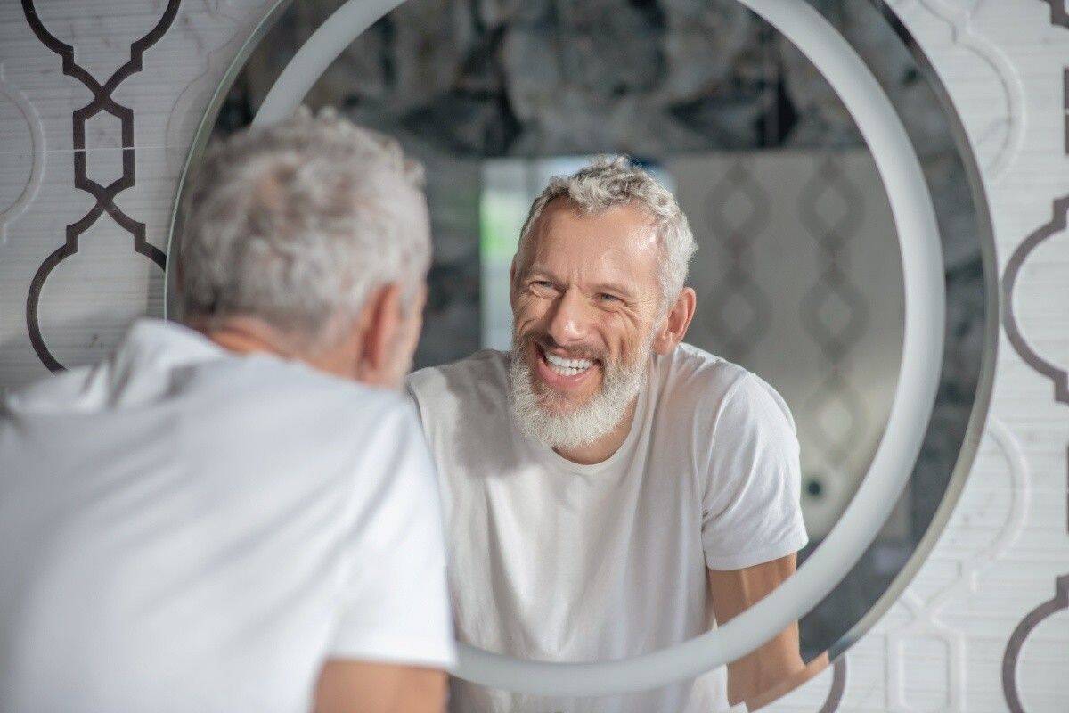 Smiling man checking his teeth in mirror, representing healthy gums and periodontal care