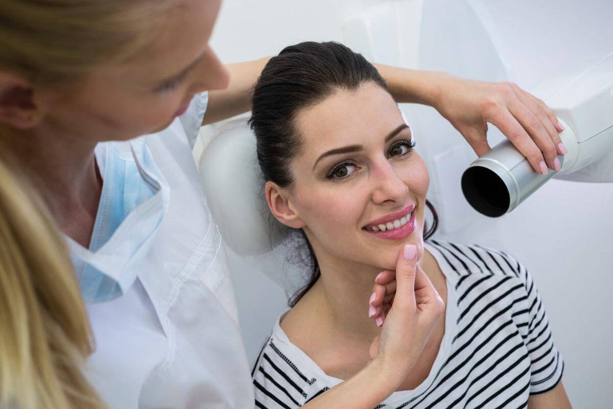 Dentist examining smiling patient’s teeth in dental clinic