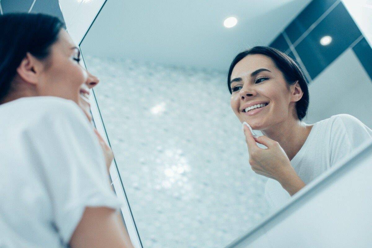 Woman smiling while checking her teeth in mirror before cosmetic veneer treatment