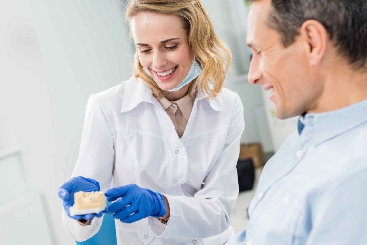 Female dentist showing a dental implant model to a male patient during an implant evaluation.